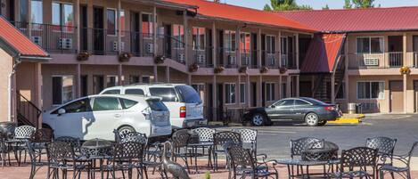 A motel with outdoor seating and multiple cars parked in front.