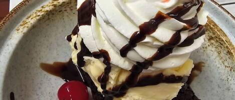 A slice of layered dessert with whipped cream, chocolate, and a cherry on top, served on a decorative plate.
