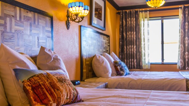 A hotel room with two beds, a patterned headboard, wall-mounted lamps, and a window with curtains. - Mountain View Lodge (Parowan)