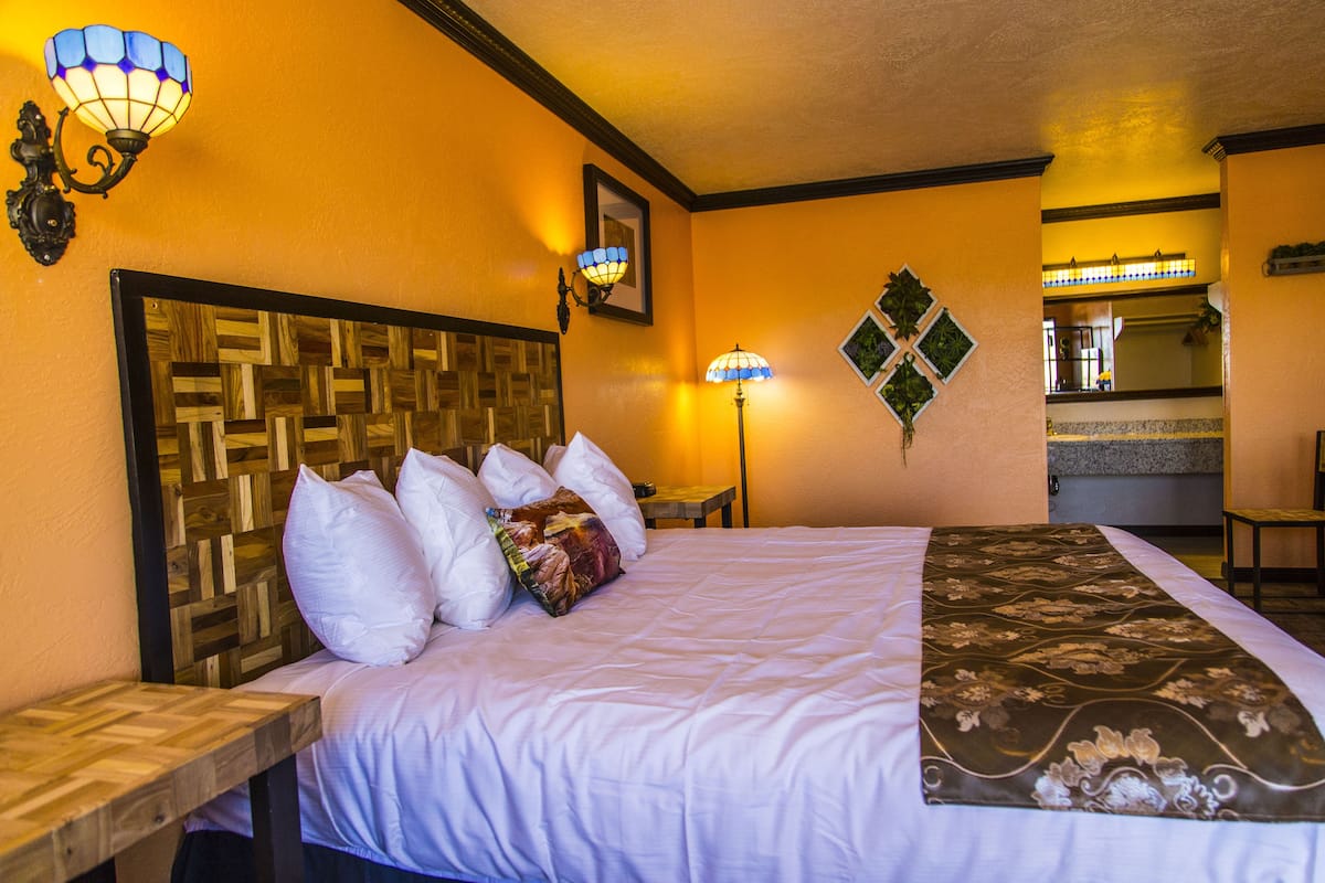 A hotel room with a wooden headboard, a bed with white and patterned bedding, two wall-mounted lamps, and a small table.