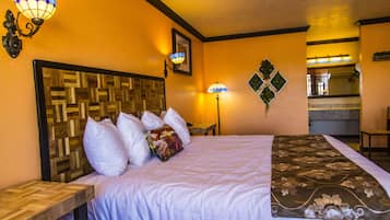 Une chambre d’hôtel avec une tête de lit en bois, un lit recouvert d’une literie blanche à motifs, deux lampes fixées au mur et une petite table.