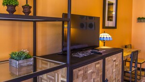 A room with a TV on a wooden cabinet, a lamp, and two potted plants on a shelf. - Mountain View Lodge (Parowan)
