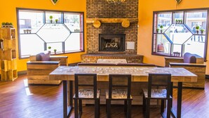 A dining area with a brick fireplace, wooden furniture, and large windows with potted plants. - Mountain View Lodge (Parowan)