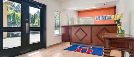 A reception area with a wooden reception desk, a blue and red carpet, and a large window with a view of trees.
