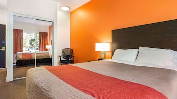A hotel room with a large bed, a nightstand with a lamp, a chair, and a sliding door leading to another room.