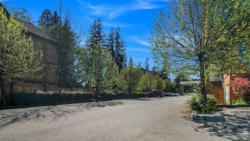 A residential street with parked cars, trees, and a building with a sloped roof.