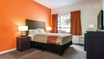 Habitación de hotel con cama, dos mesitas de noche con lámparas, televisión y ventana con cortinas.