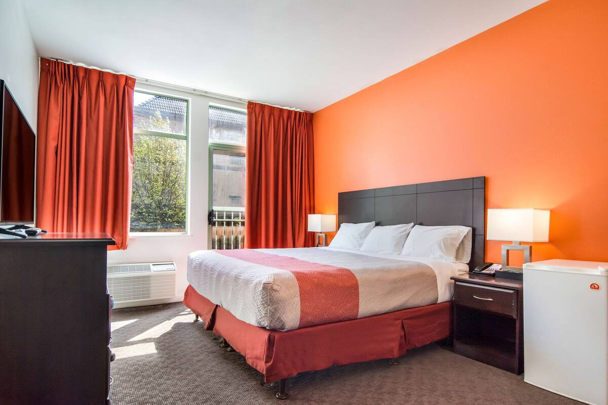 A hotel room with a bed, nightstands, a desk, and a refrigerator.