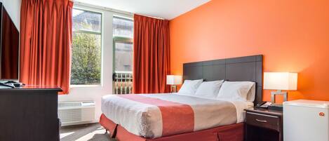 A hotel room with a bed, nightstands, a desk, and a refrigerator.