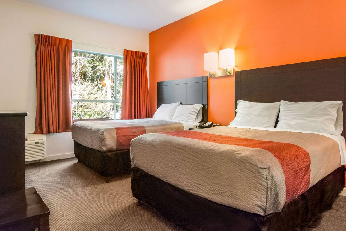 A hotel room with two beds, a window with curtains, and a nightstand with a lamp.