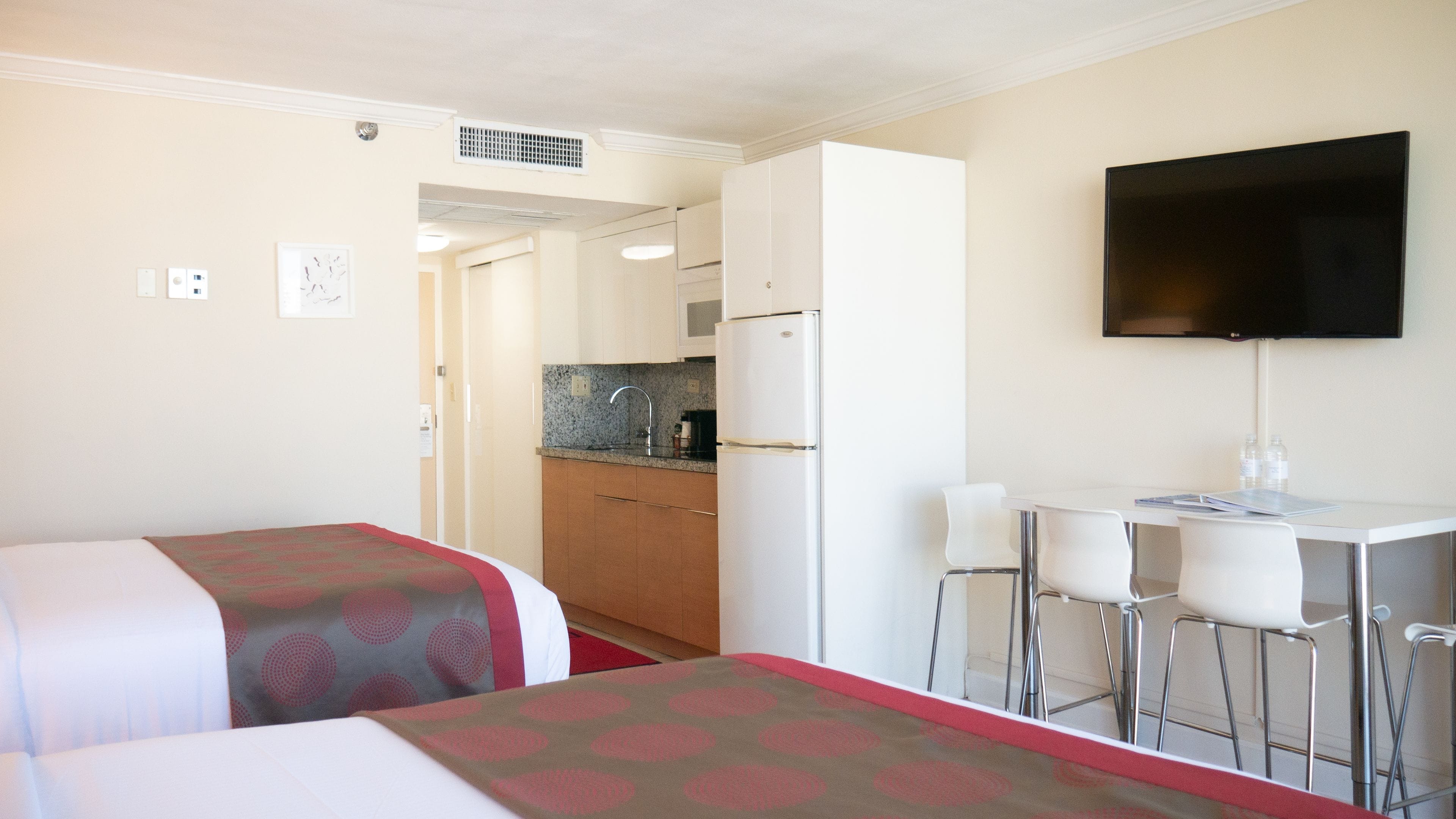 A hotel room with two beds, a kitchenette, a TV, and a small dining area.