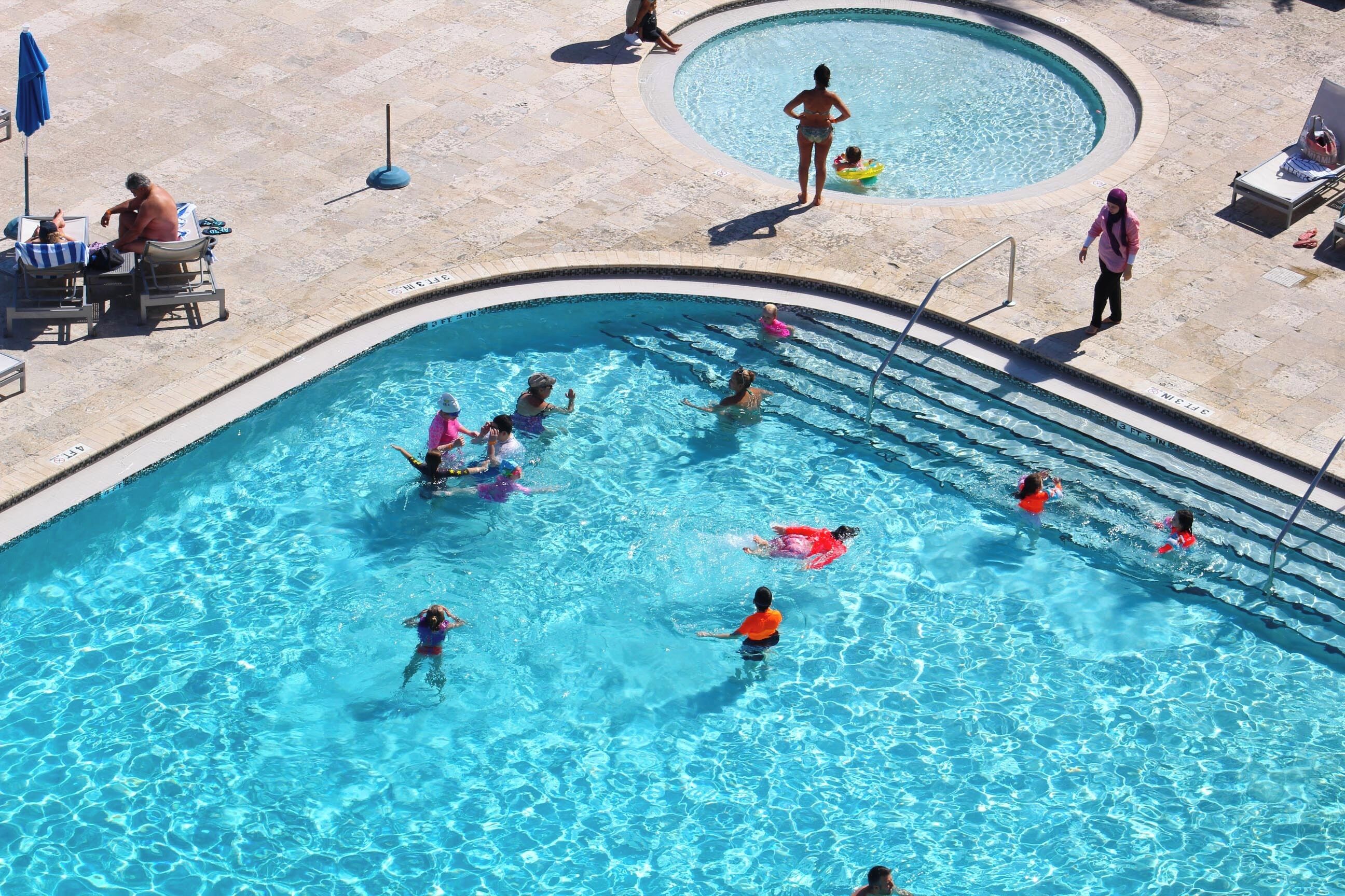 Une piscine où se trouvent plusieurs personnes, dont des enfants et des adultes, qui nagent et s’amusent.