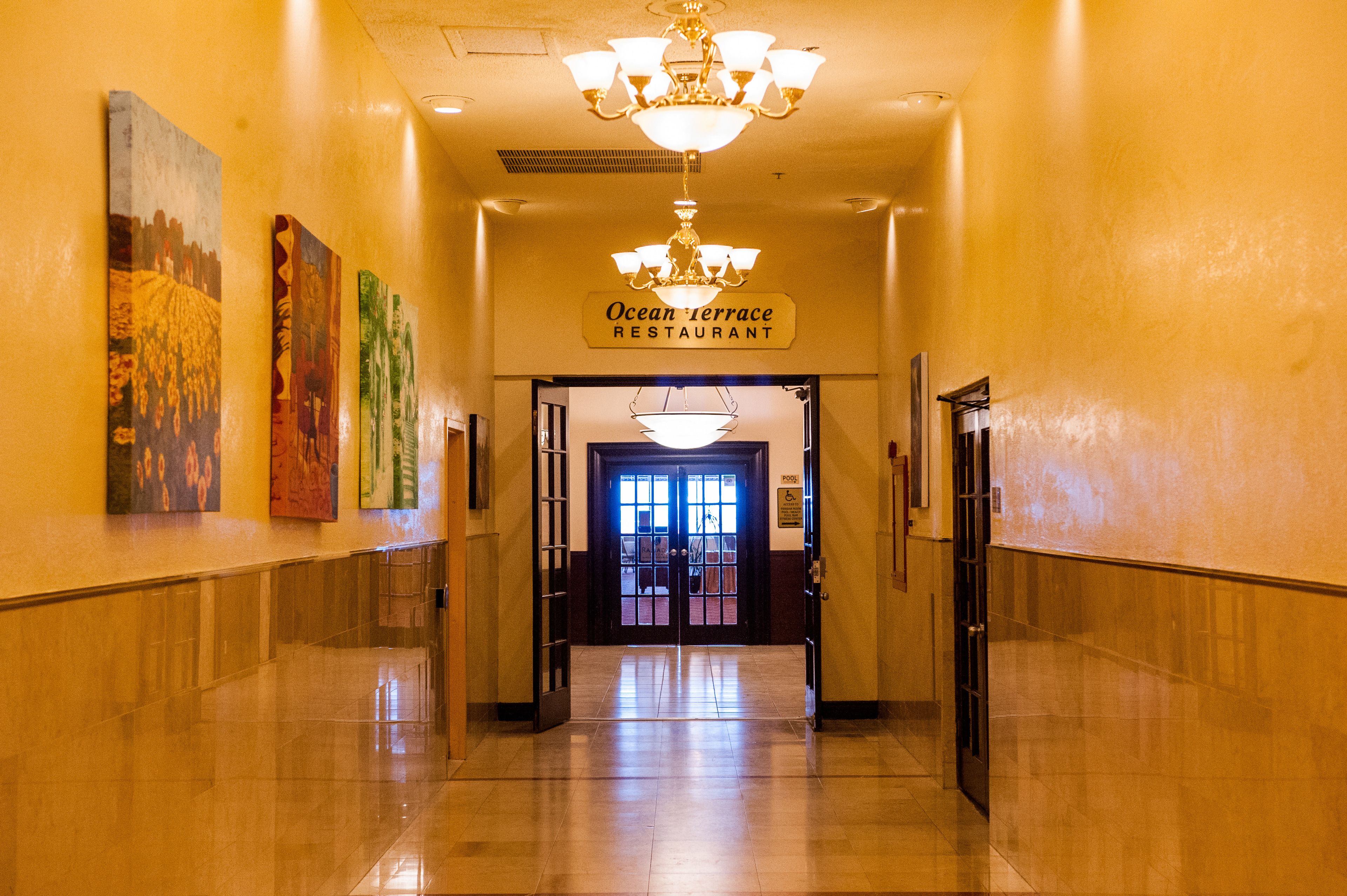 A hallway with a sign for Ocean Terrace Restaurant, a chandelier, and artwork on the walls.