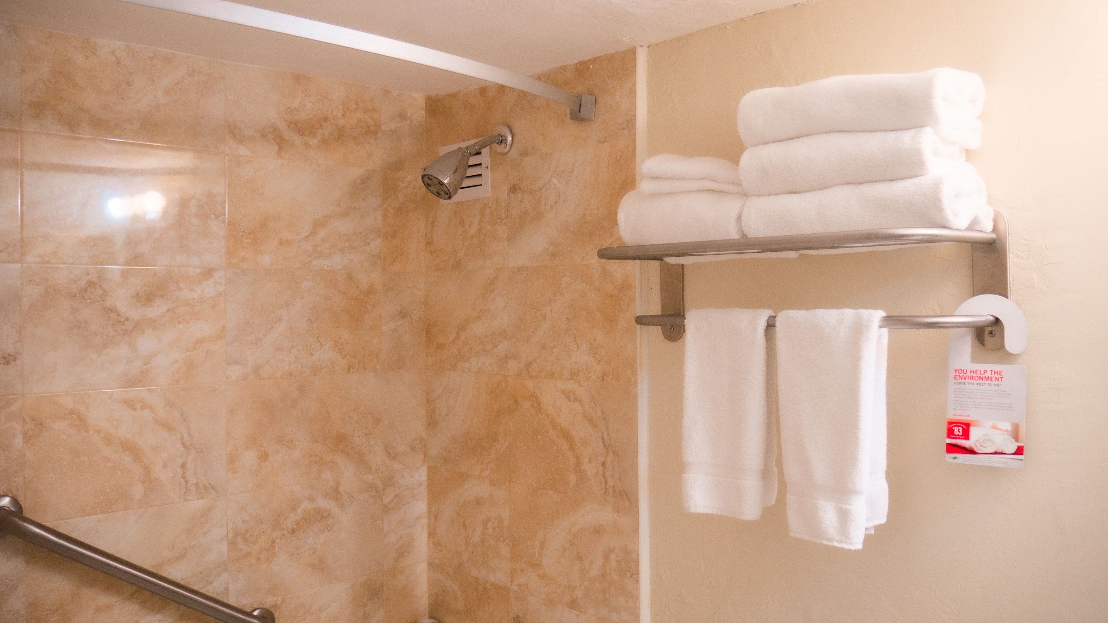 Ein Badezimmer mit Dusche, einem Handtuchhalter mit gefalteten Handtüchern und einem Schild zur Förderung des Umweltbewusstseins.