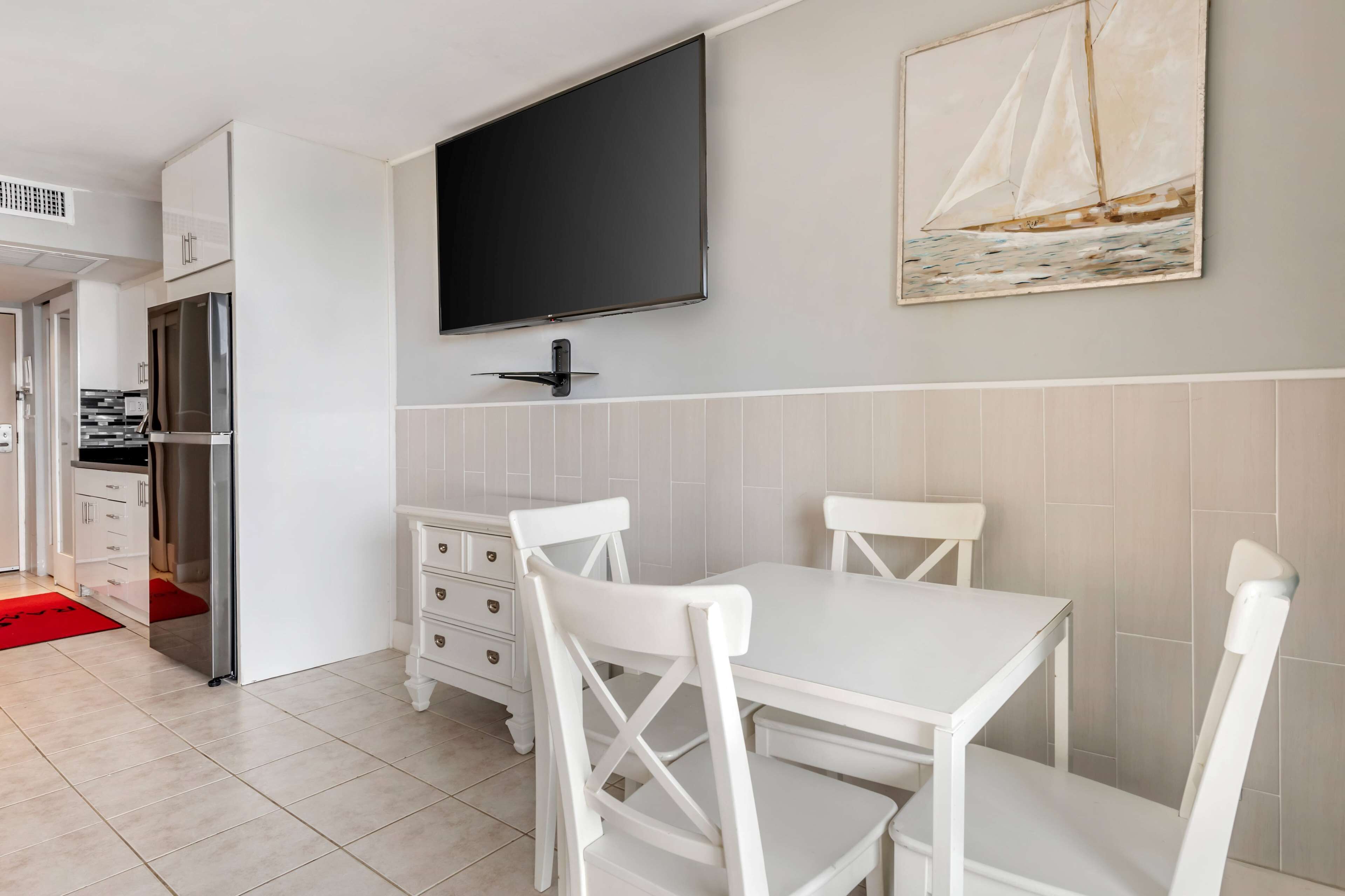 A modern kitchen with white cabinets, a built-in oven, and a flat-screen TV mounted above the counter.