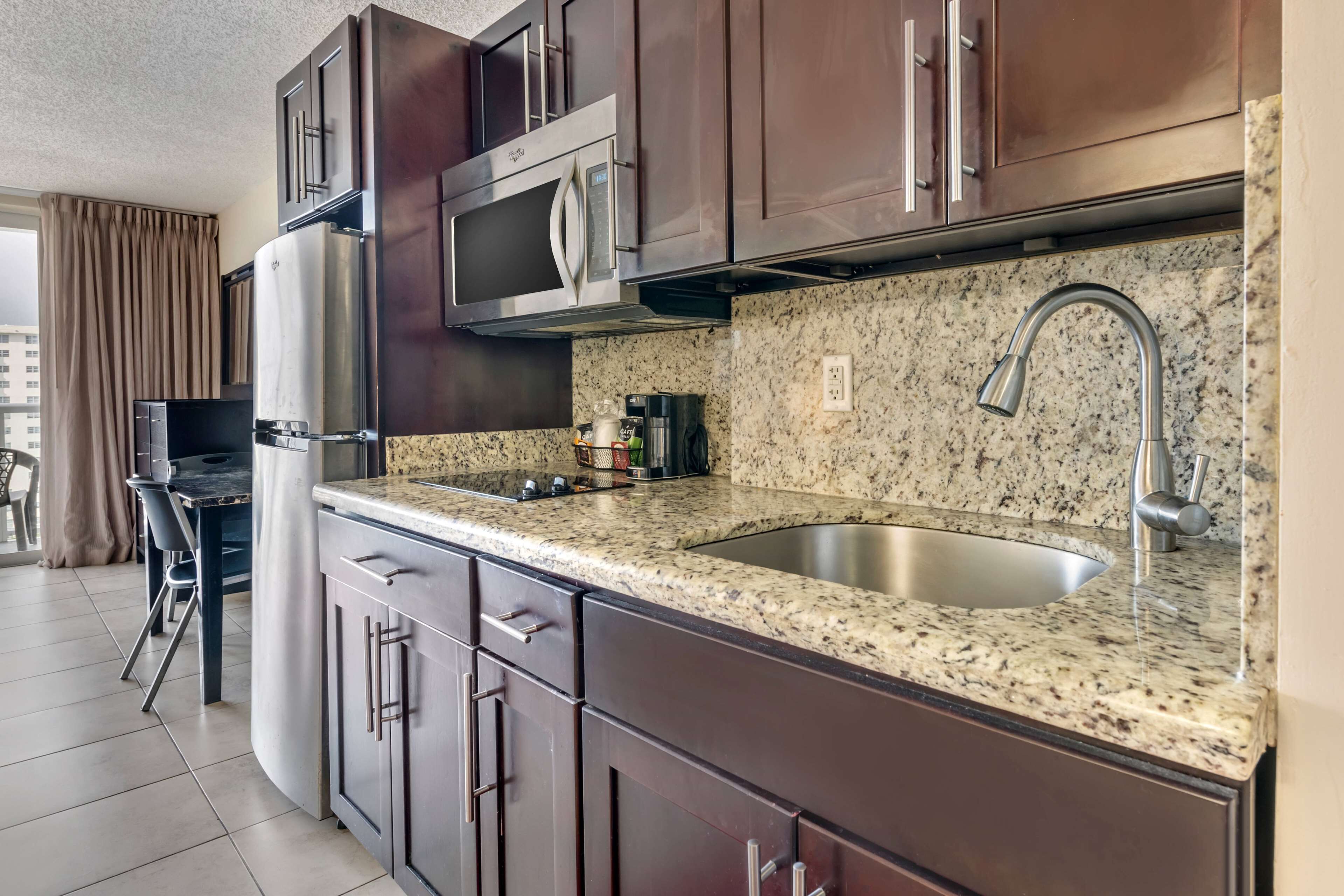 A modern kitchen with dark wooden cabinets, stainless steel appliances, a granite countertop, and a built-in sink.