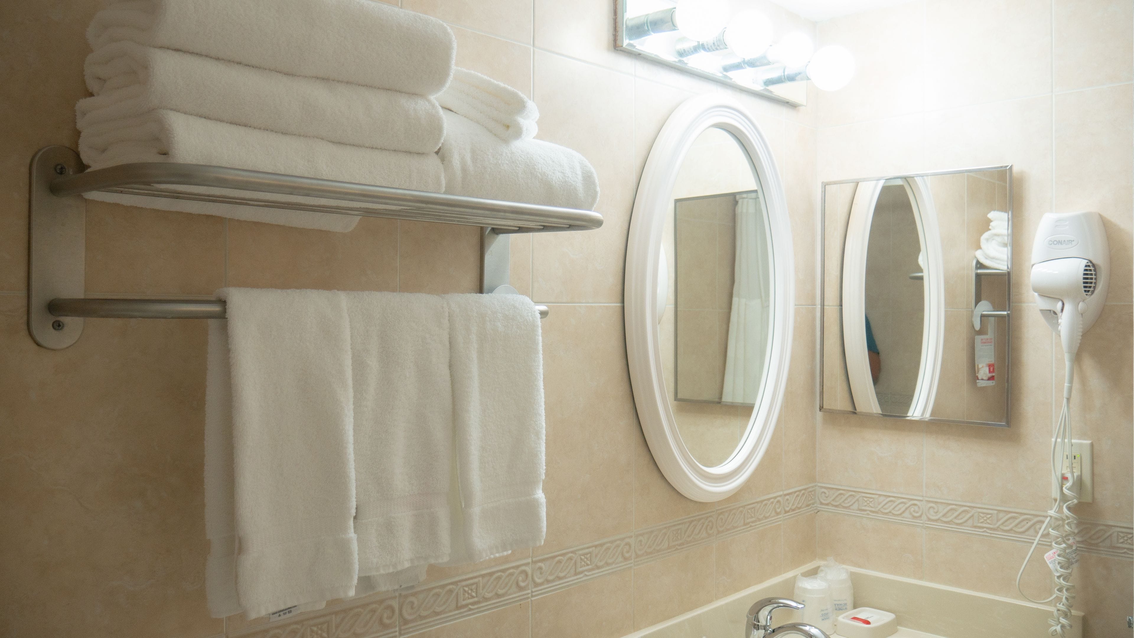A bathroom with a towel rack holding folded towels, a mirror, and a hair dryer on the wall.