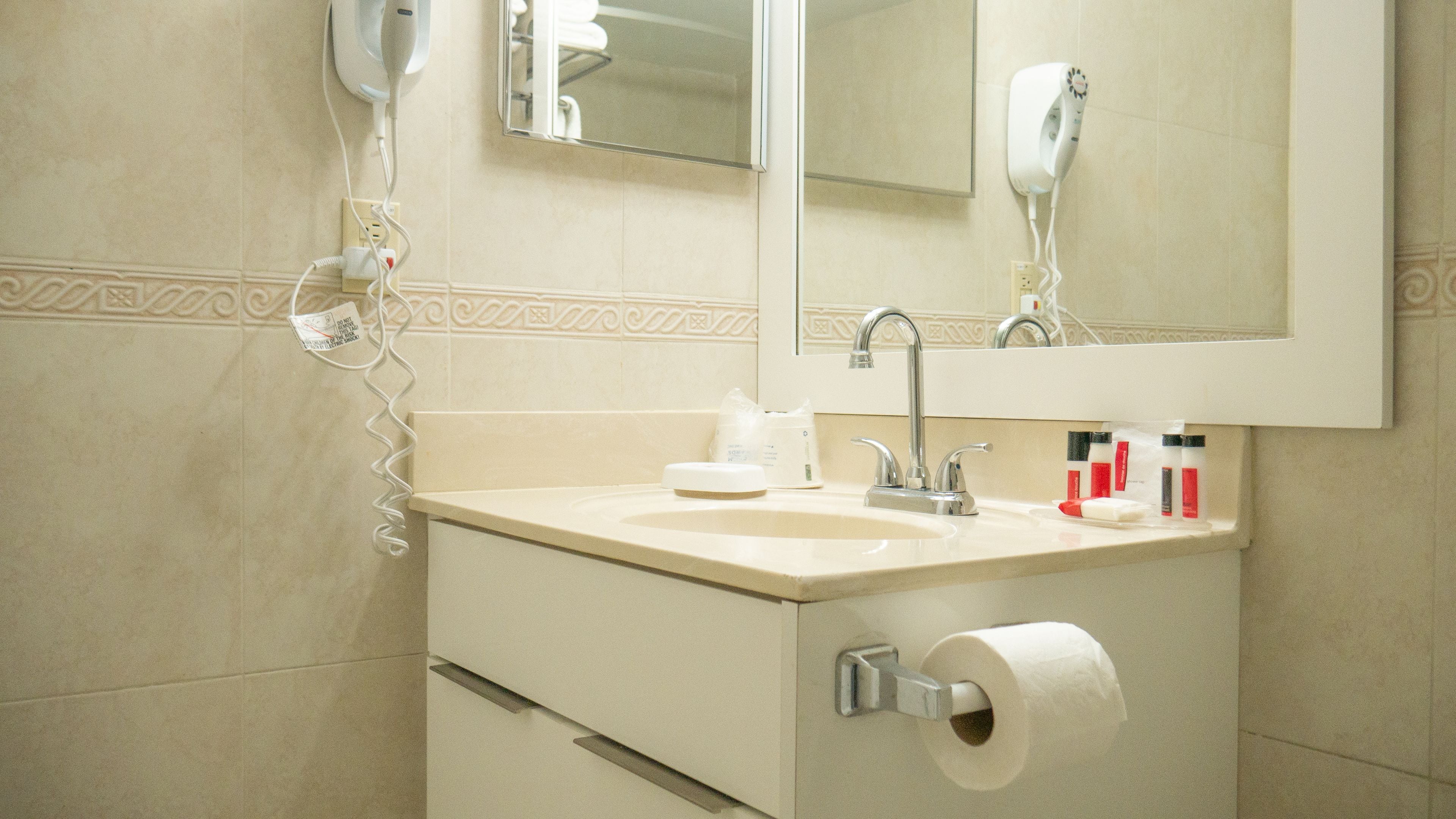 A bathroom with a sink, mirror, towel dispenser, and toilet paper.