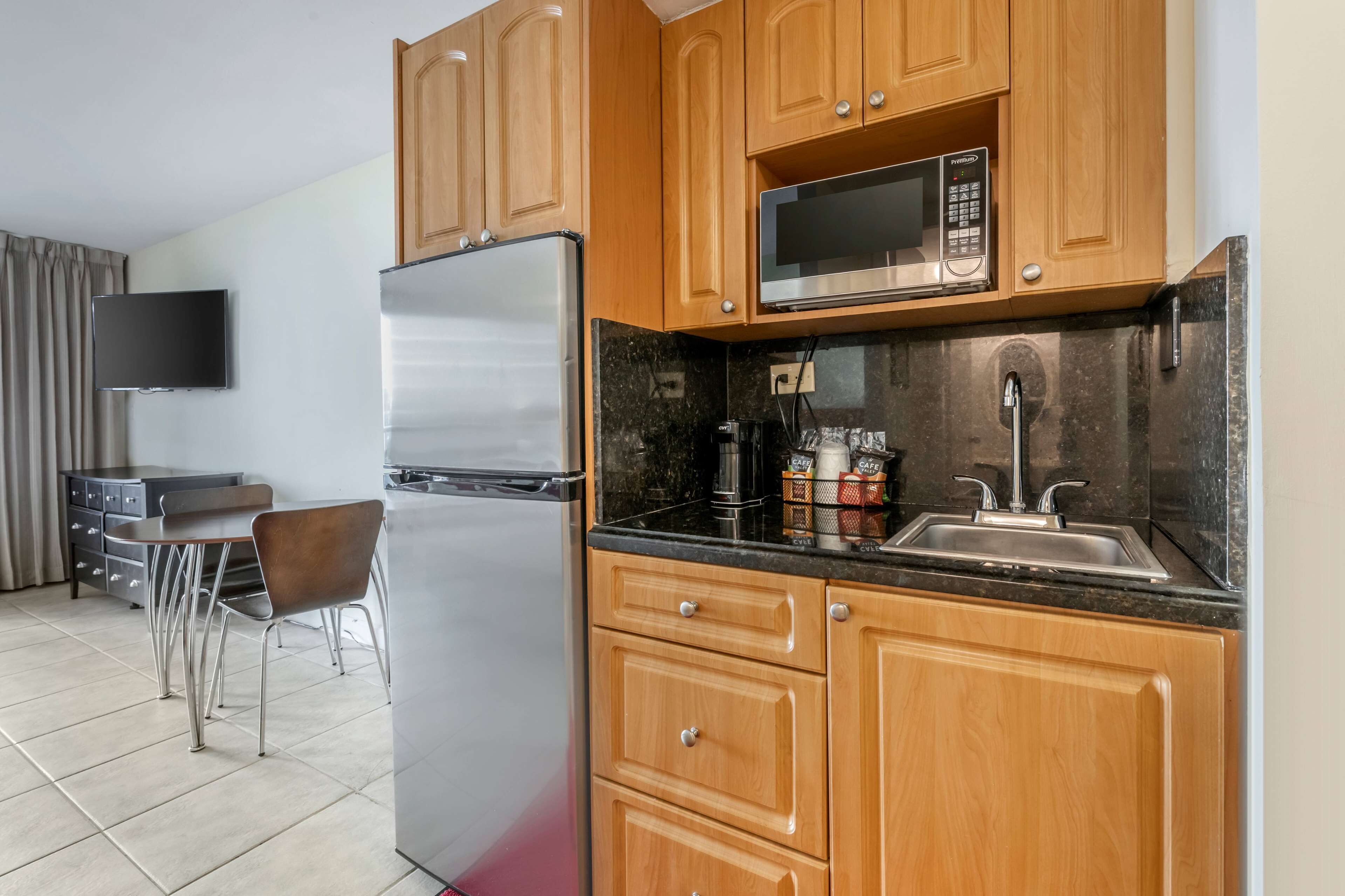 A modern kitchen with wooden cabinets, a stainless steel refrigerator, a microwave, and a sink.