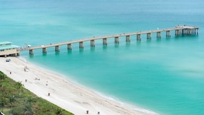 Un muelle se adentra en aguas turquesas, con una playa y un edificio a la izquierda.