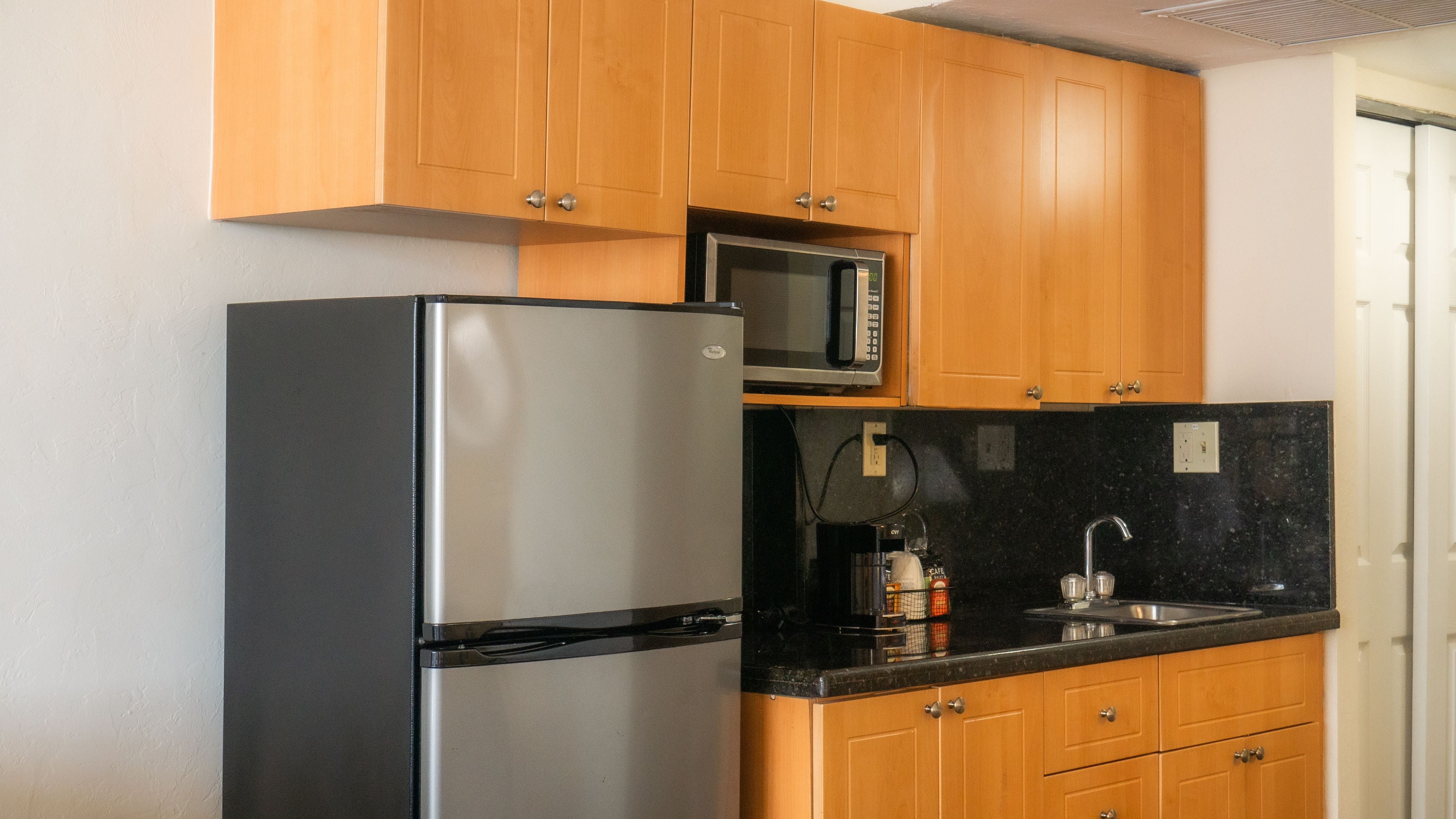 Una cocina compacta con armarios de madera, un refrigerador de acero inoxidable, un microondas y una encimera negra.