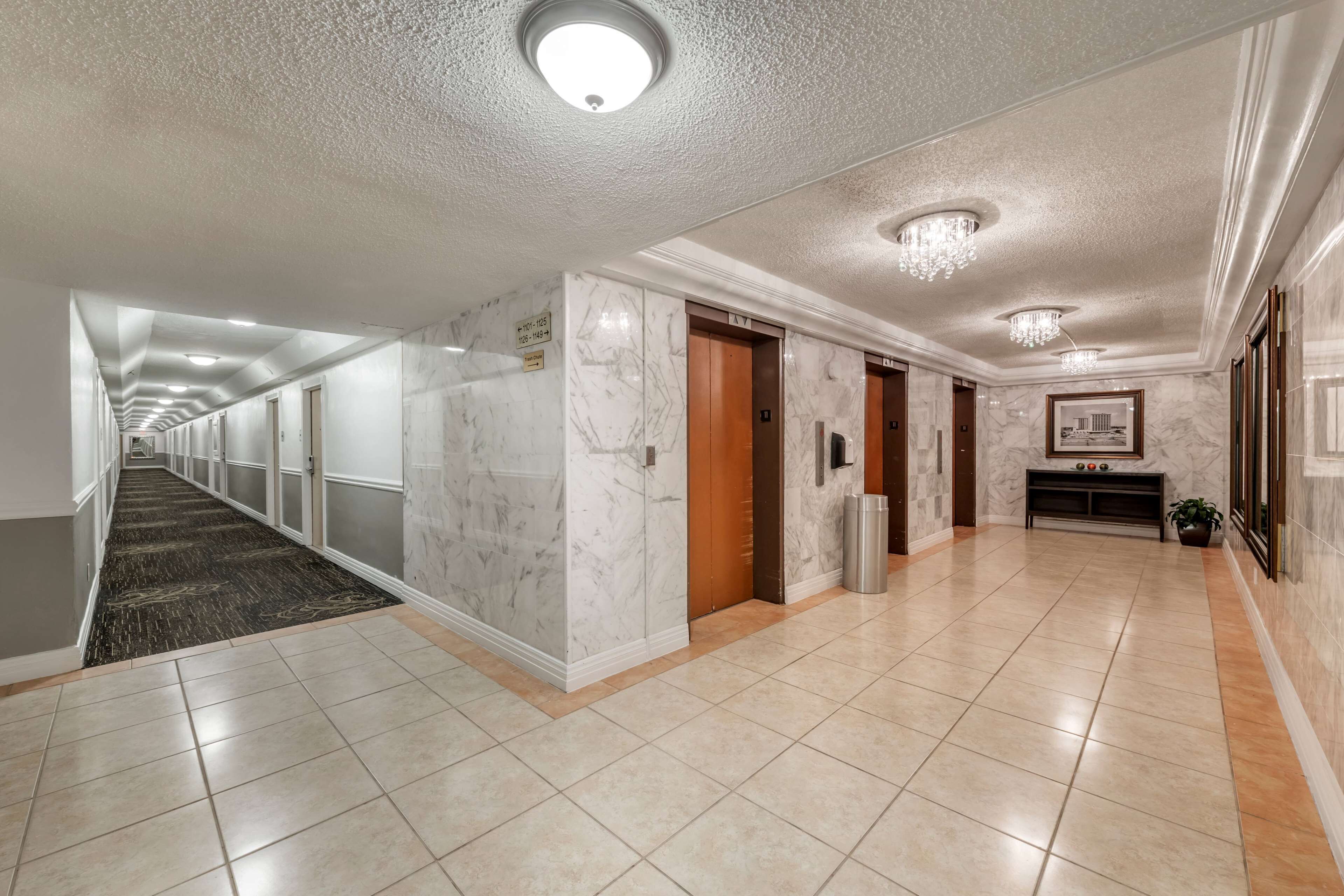 A hotel corridor with marble walls, tiled floors, and wooden doors.