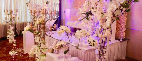 A wedding reception area with white floral arrangements, a chandelier, and a tiered cake on a table.