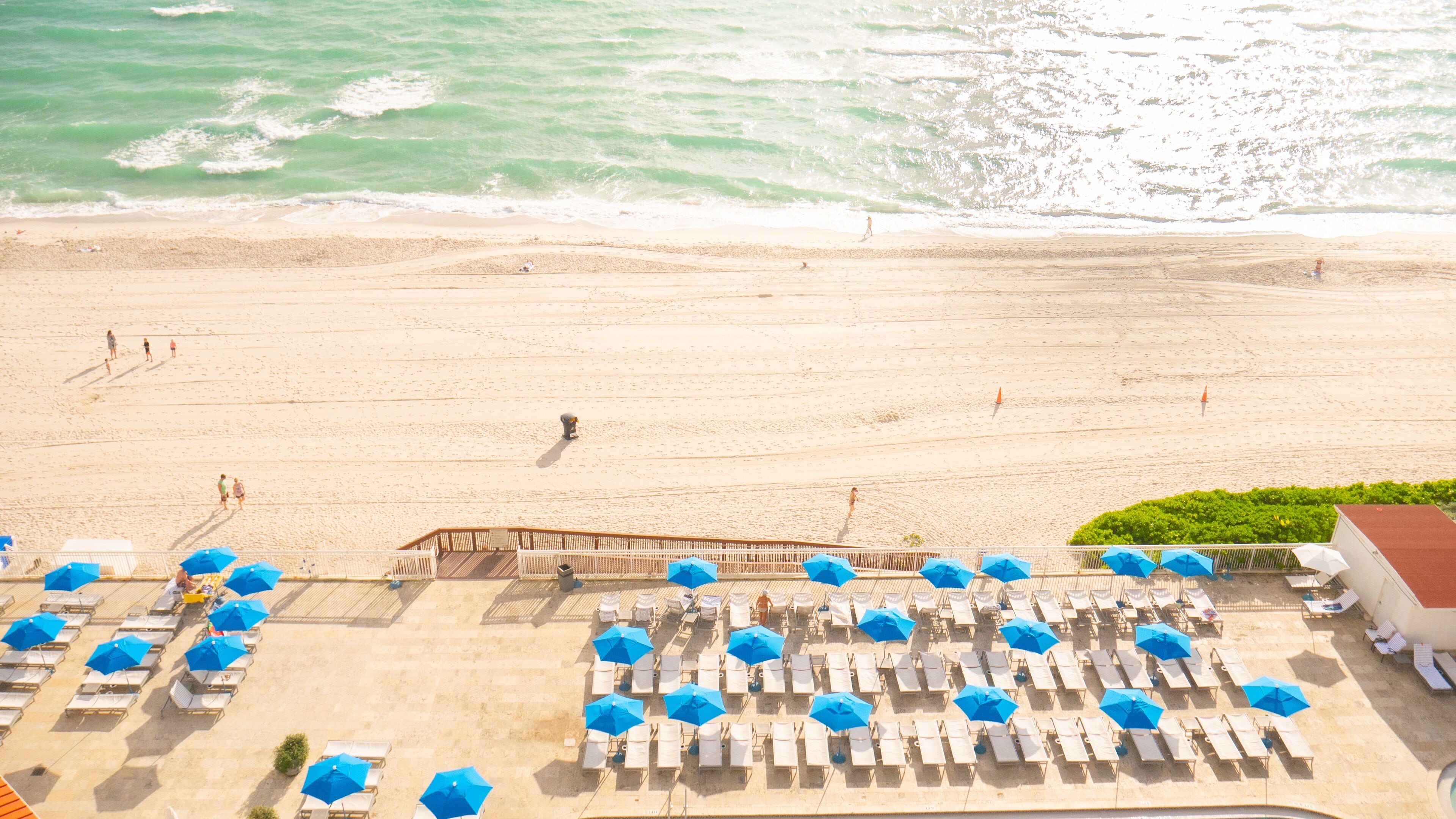 Un complexe hôtelier de bord de mer doté de chaises longues et de parasols, d’une terrasse en bois et offrant une vue sur l’océan.