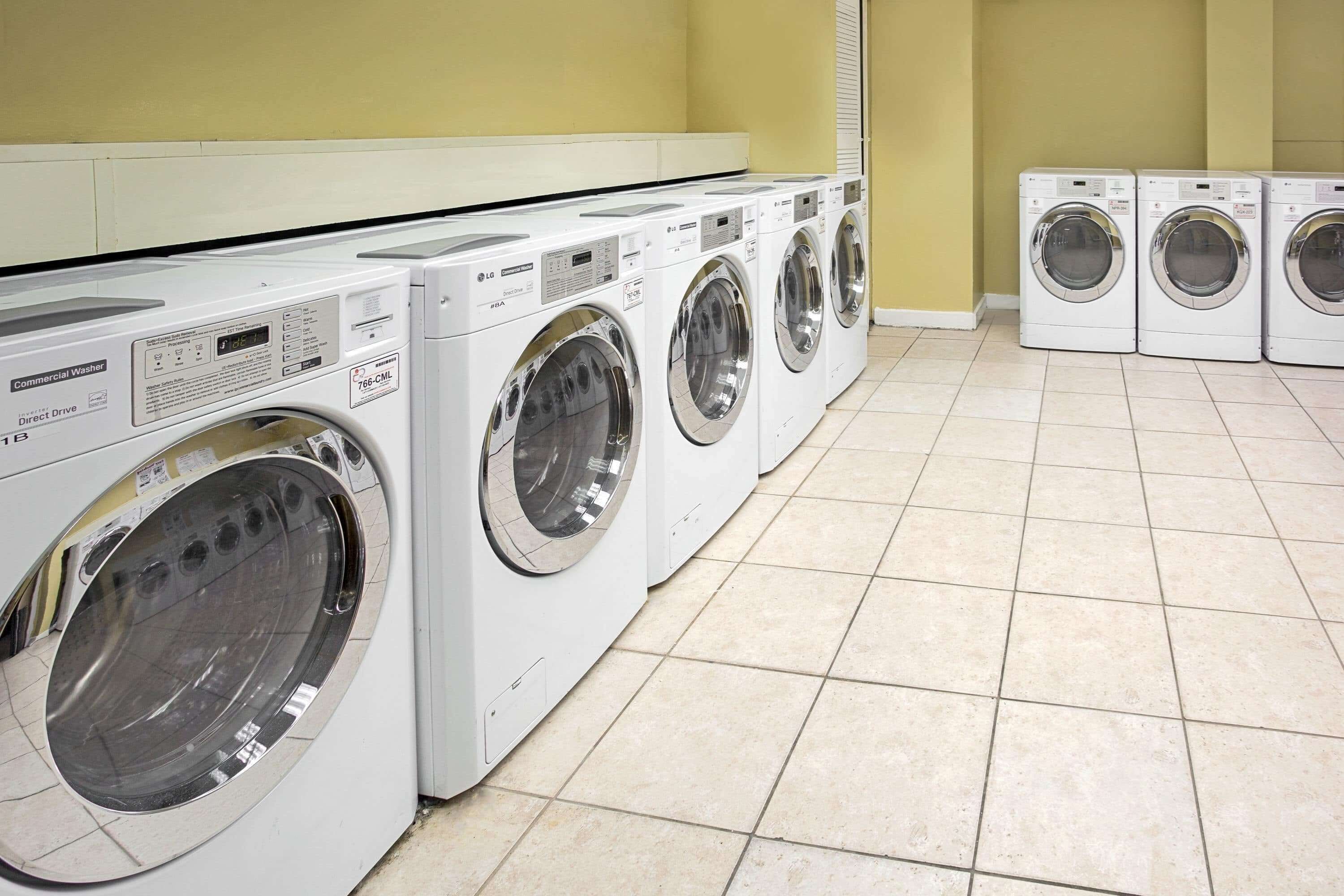 A row of commercial washers in a laundry room with tiled flooring.