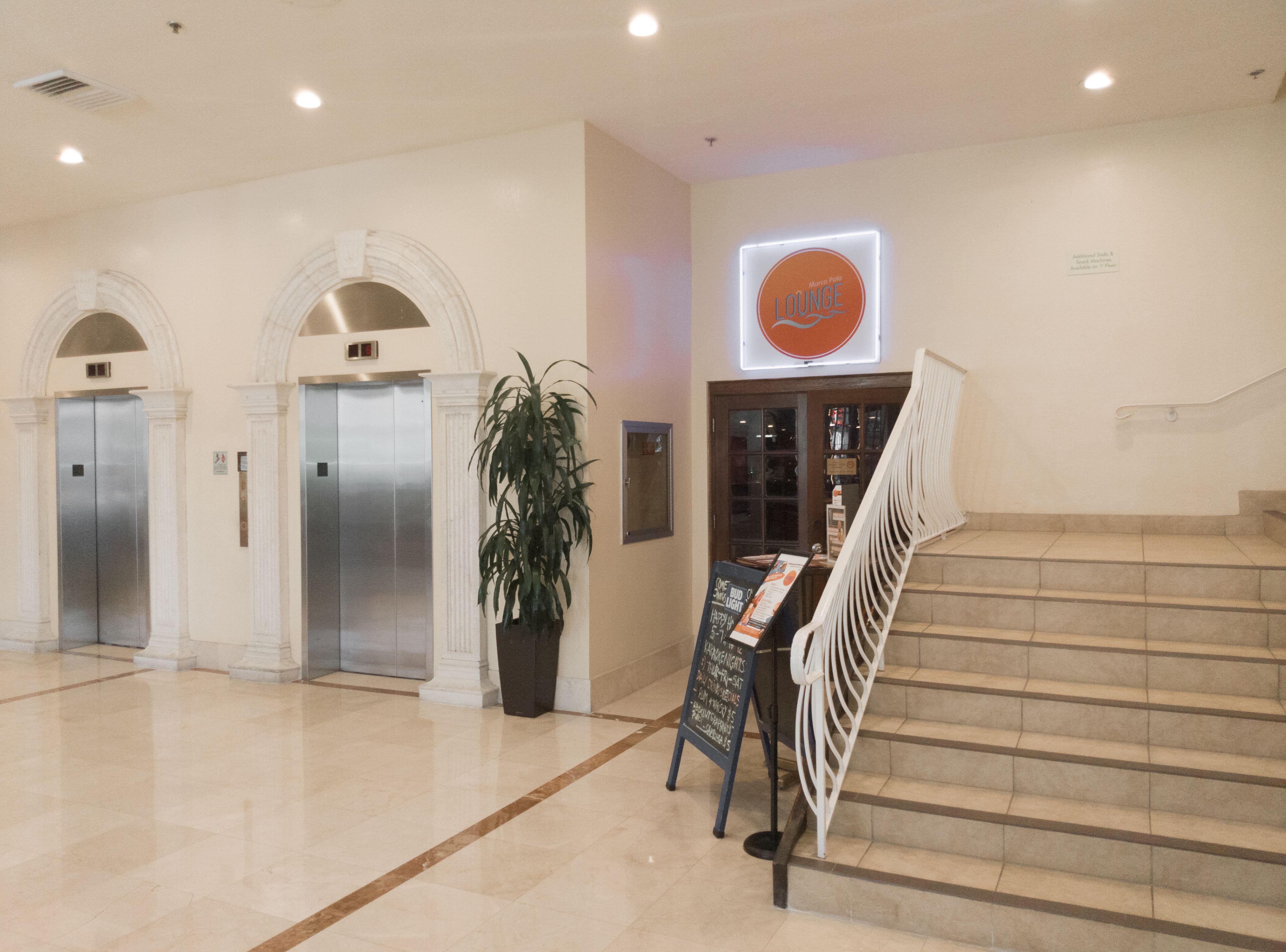A lobby with two elevators, a staircase, and a sign for a lounge.