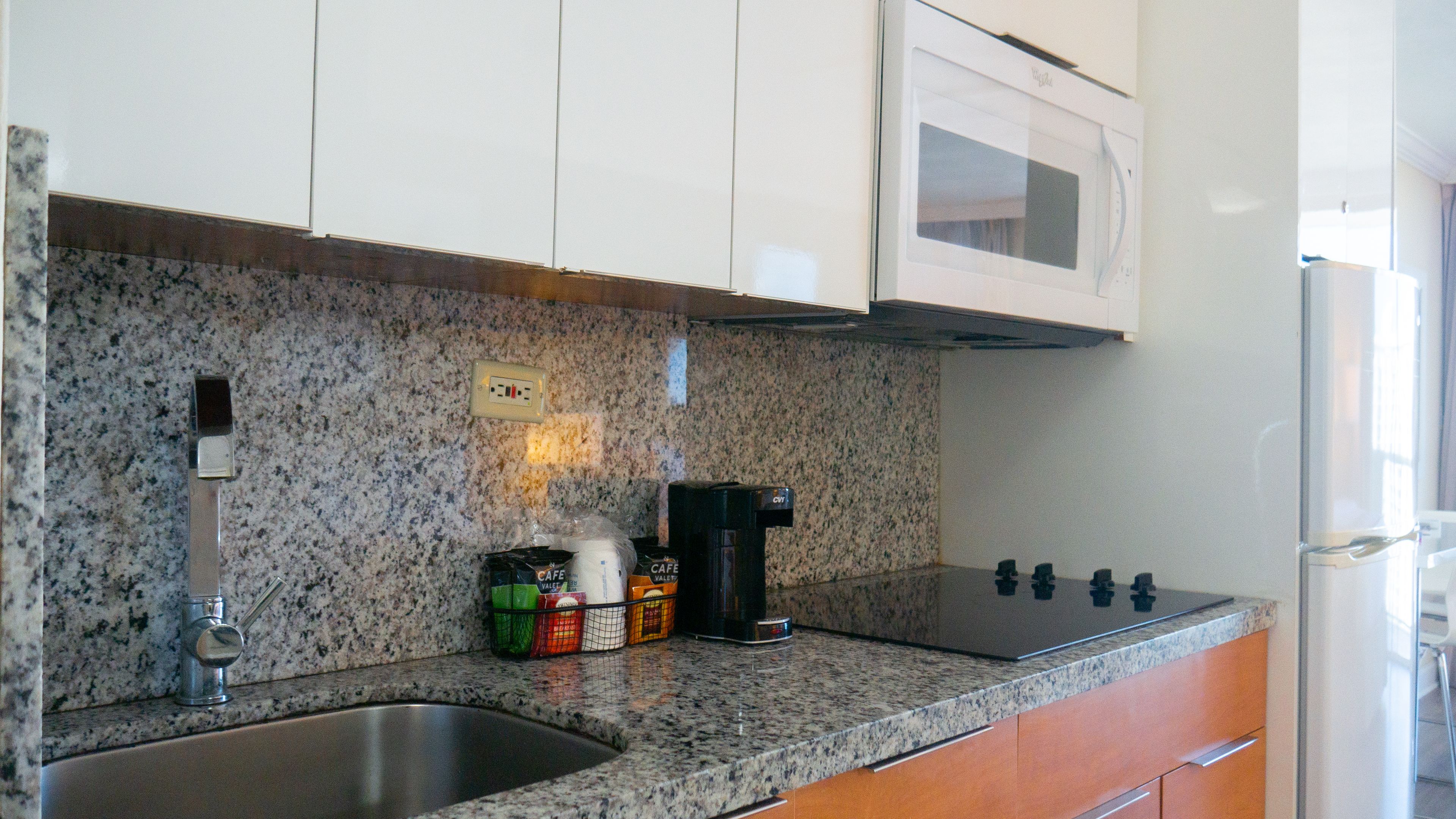 A kitchen with granite countertops, a stainless steel sink, a coffee maker, and a microwave.