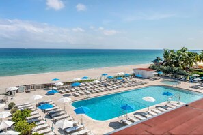A poolside area with lounge chairs and umbrellas, a swimming pool, and a beach view. - Ramada Plaza by Wyndham Marco Polo Beach Resort (Sunny Isles Beach)