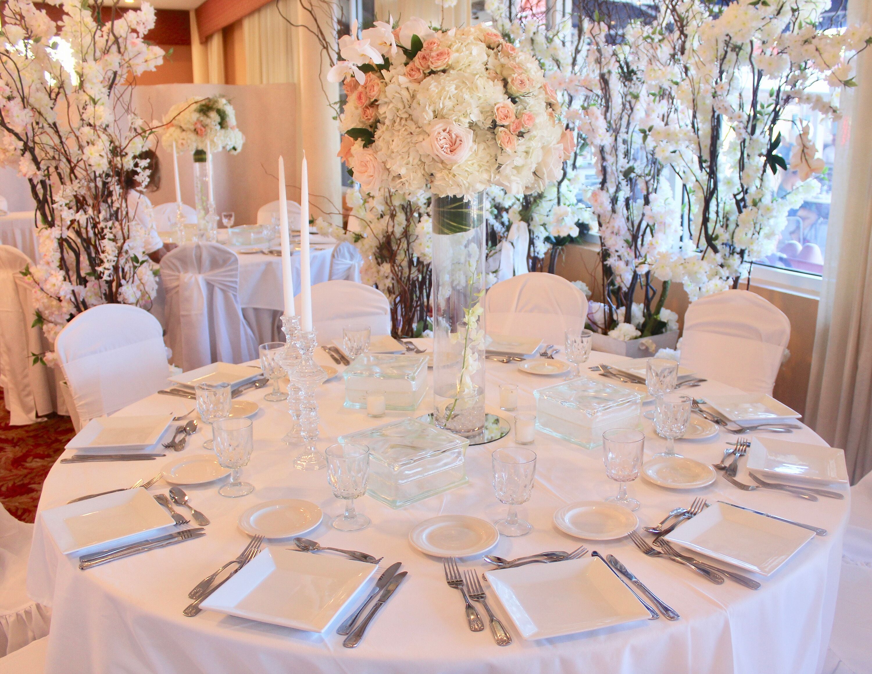 Una mesa redonda dispuesta para un evento formal, con manteles blancos, cristalería y cubertería.