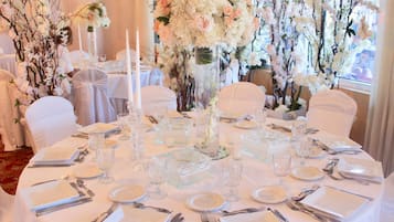 Una mesa redonda dispuesta para un evento formal, con manteles blancos, cristalería y cubertería.