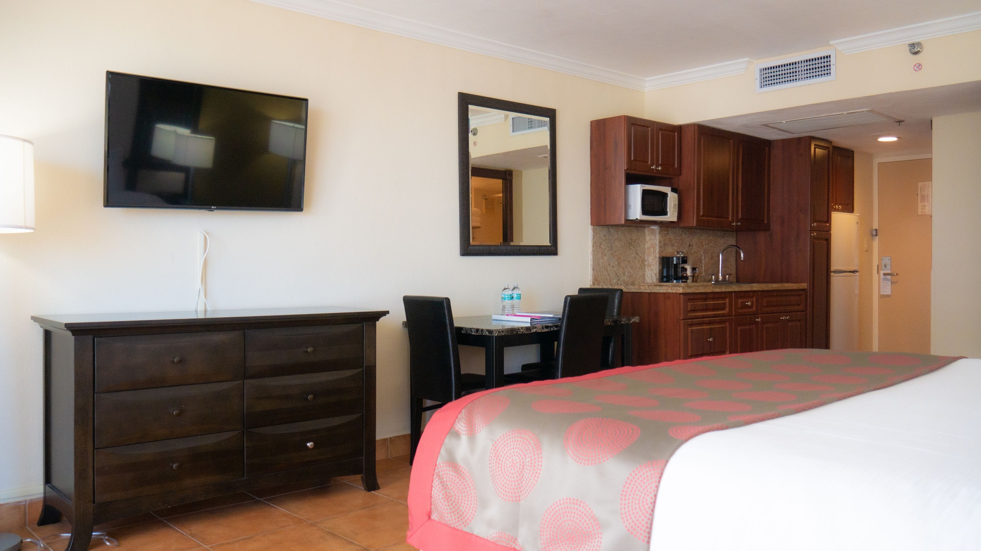A hotel room with a bed, a desk, a dresser, a television, a microwave, and a kitchen area.