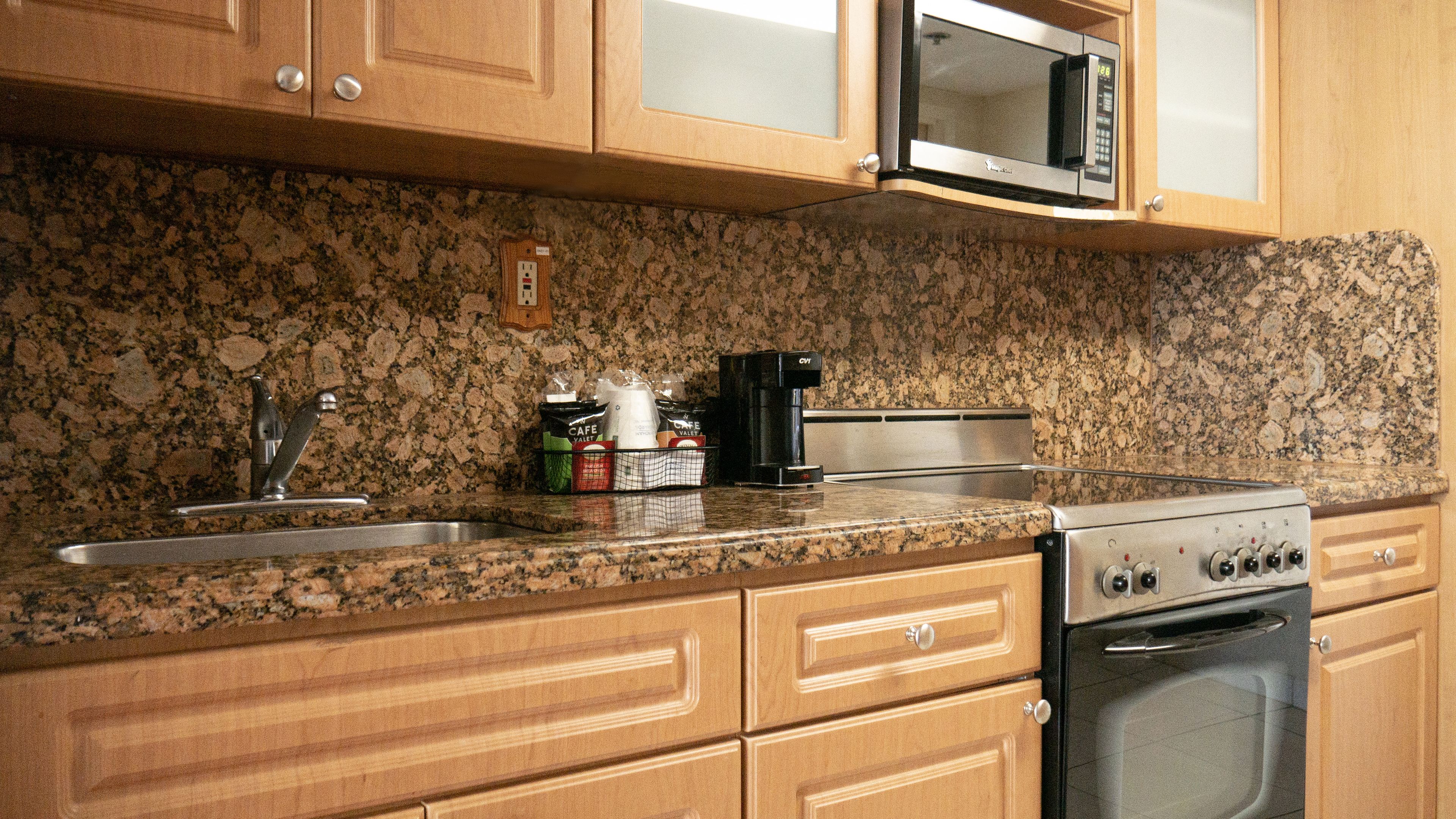 A kitchen with granite countertops, wooden cabinets, a stainless steel stove, a microwave, and a coffee maker.