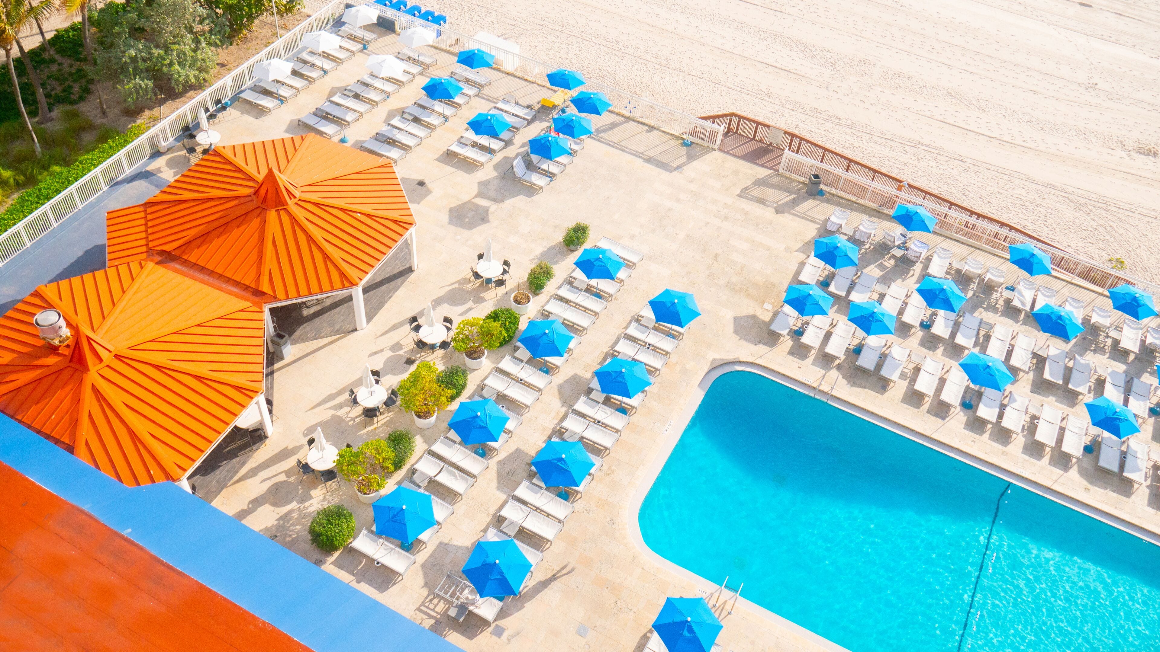 Vue aérienne d’un complexe hôtelier avec une piscine, des chaises longues et des parasols.