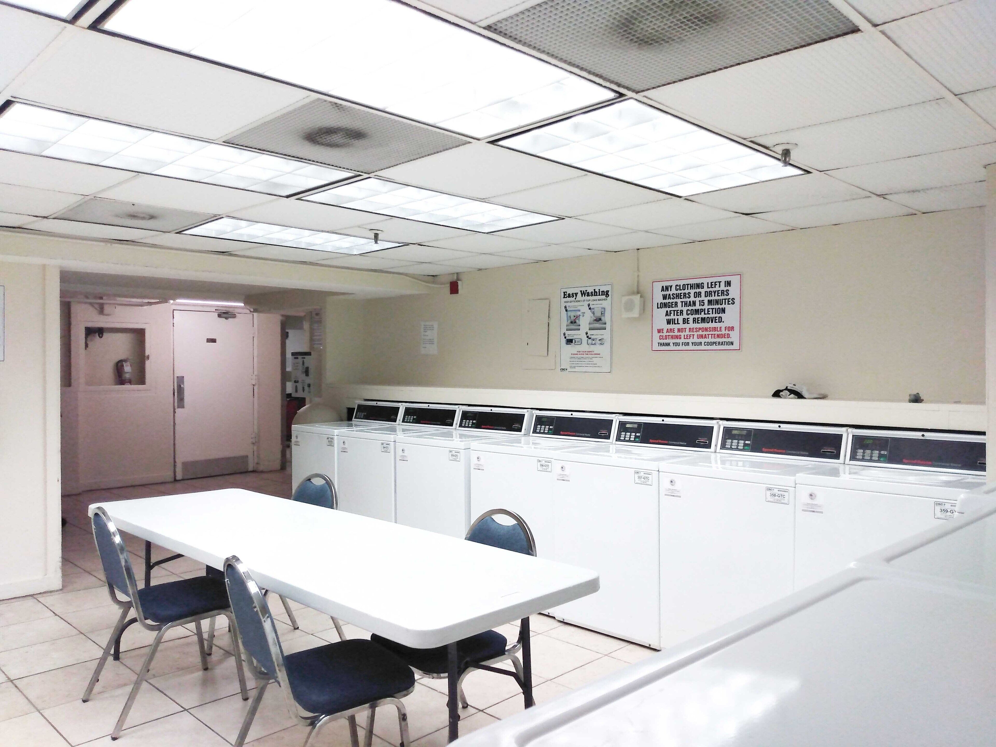 A laundromat with multiple washing machines, a table, and chairs.