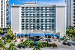 A large hotel with multiple floors, a covered parking area, and a view of the ocean. - Ramada Plaza by Wyndham Marco Polo Beach Resort (Sunny Isles Beach)