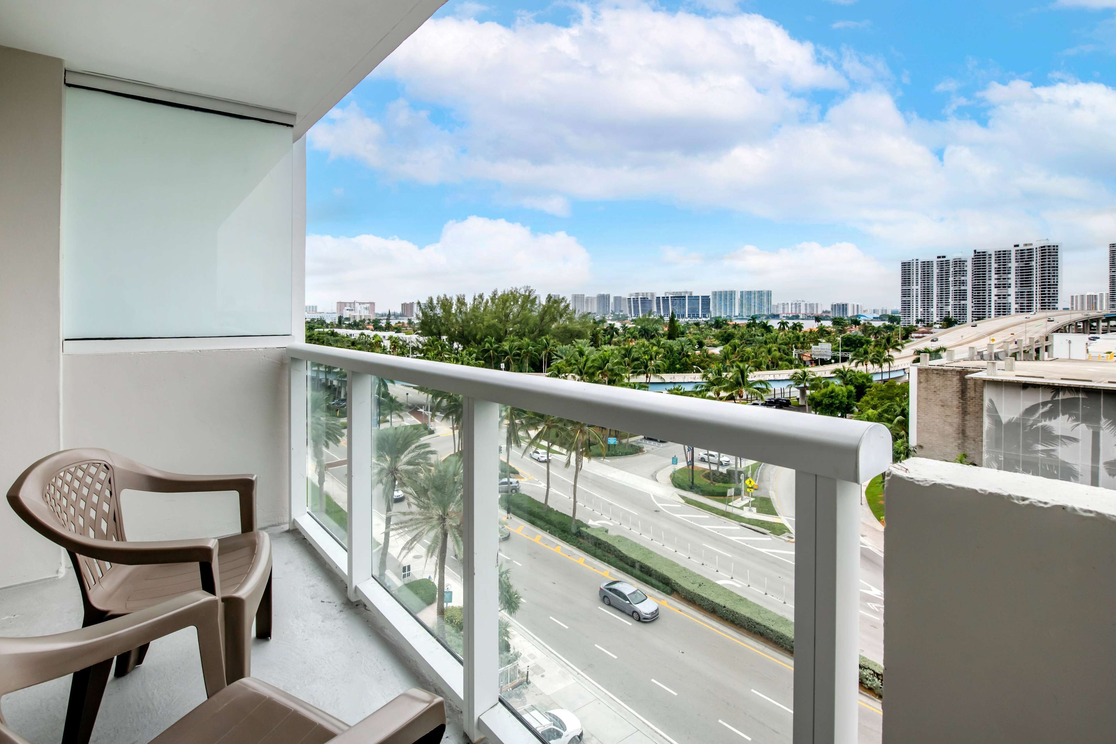 A balcony with a view of a cityscape, including high-rise buildings and a road with cars.