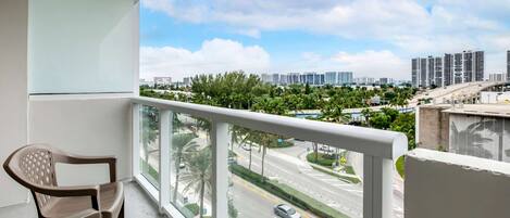 A balcony with a view of a cityscape, including high-rise buildings and a road with cars.