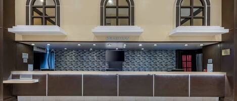 A reception area with a reception desk, three arched windows, a tiled wall, and a flat-screen TV.