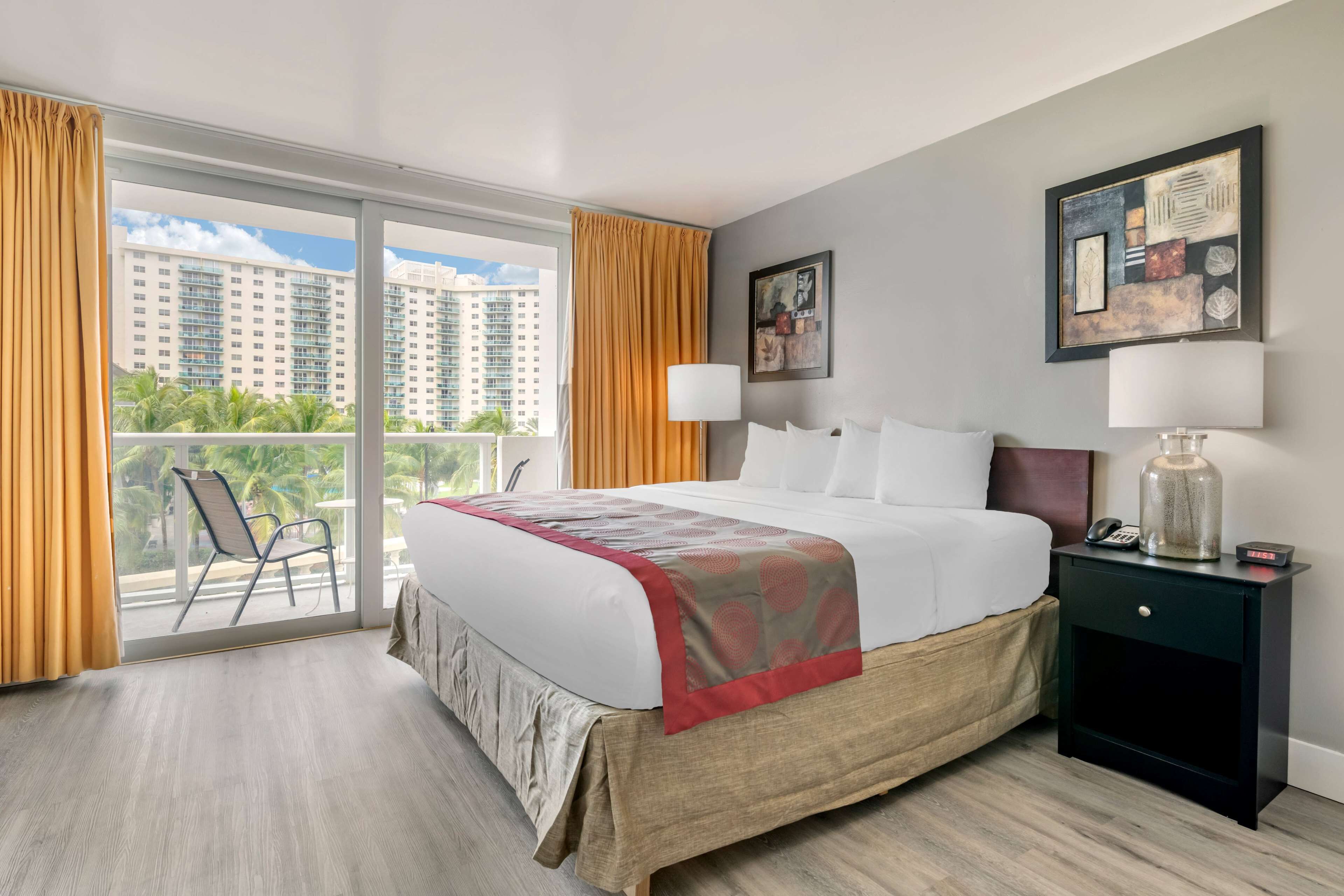 Une chambre d’hôtel avec un grand lit, une table de chevet, une chaise et un balcon offrant une vue sur les immeubles de grande hauteur.