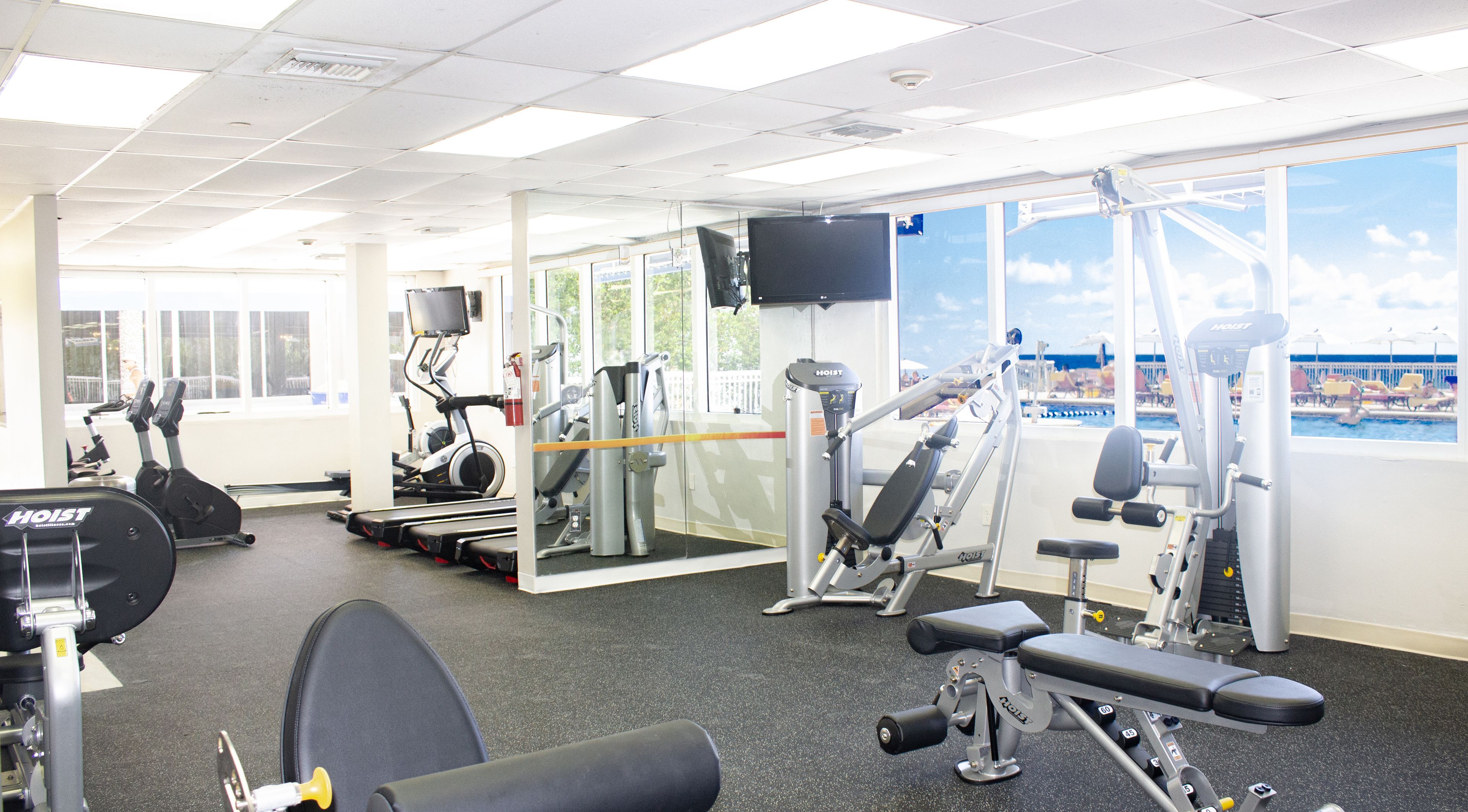 A gym with various exercise equipment, large windows, and a view of a pool area.