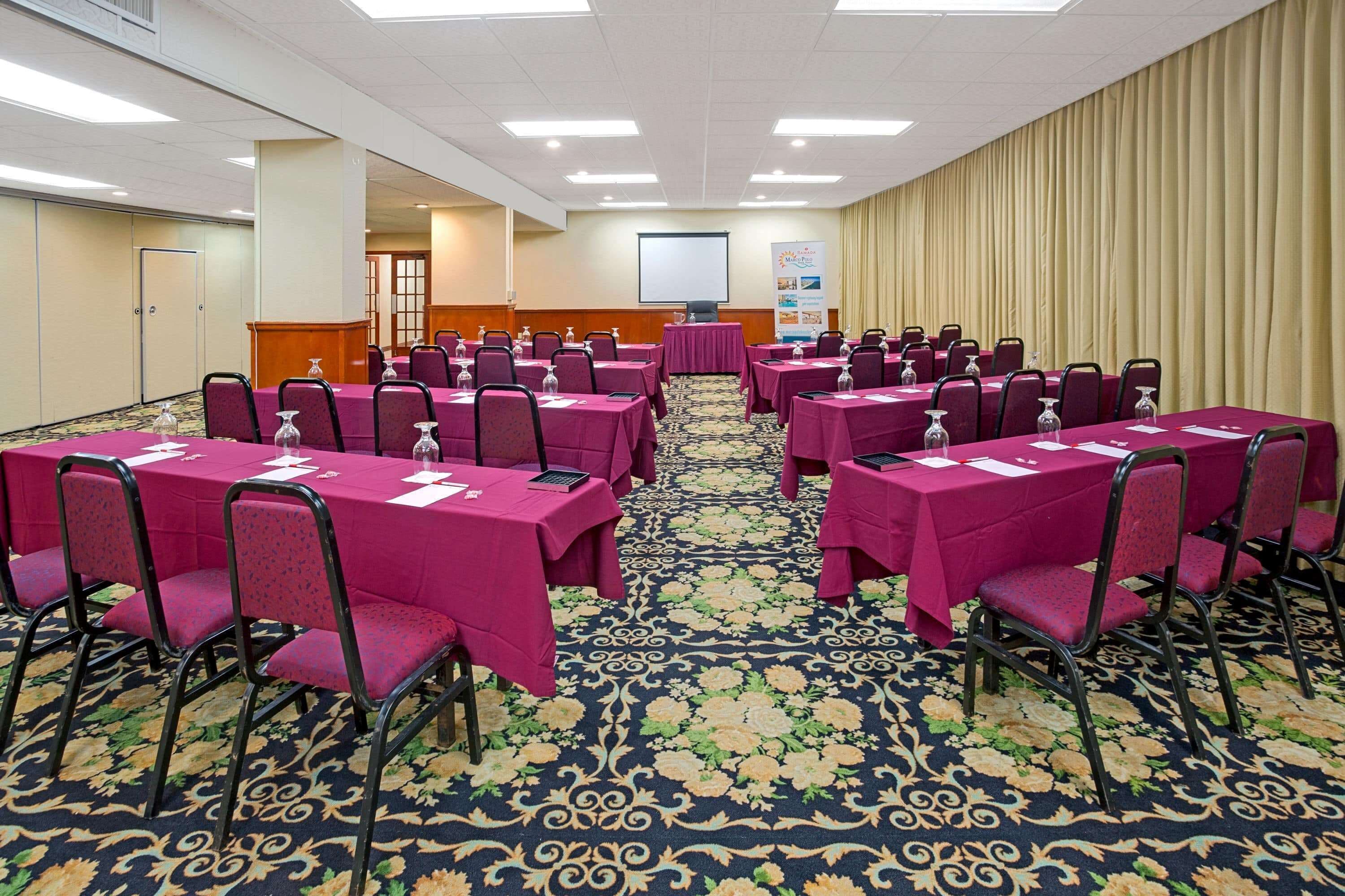 A conference room with multiple tables and chairs, a carpeted floor, and a projector screen on the wall.