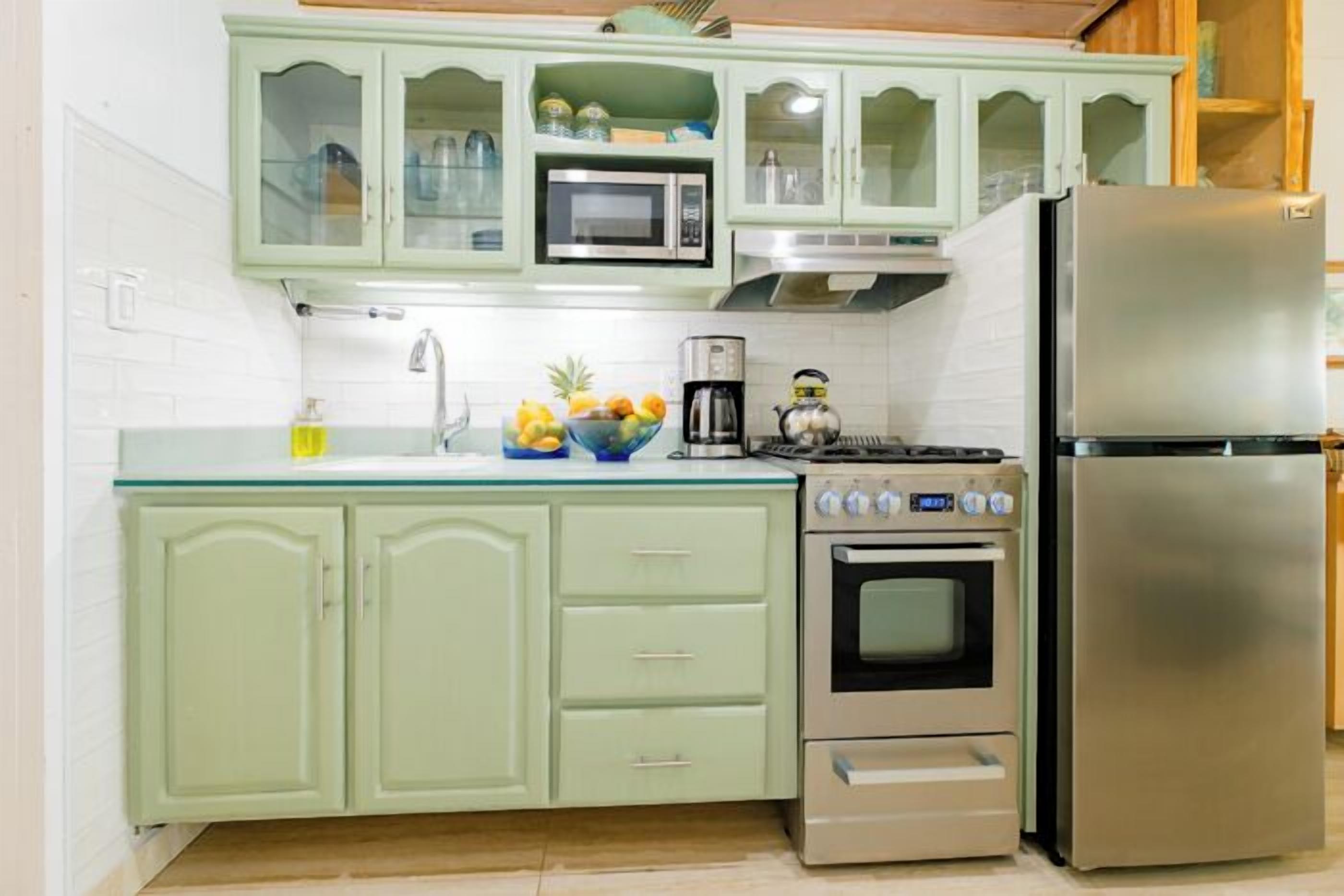 A kitchen with light green cabinets, a stainless steel refrigerator, a microwave, an oven, and a sink.