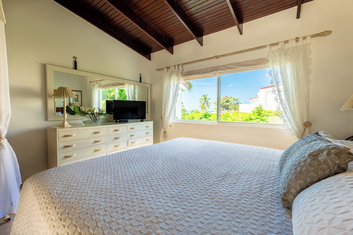 Une chambre à coucher comprenant un lit, une commode, un téléviseur et une fenêtre donnant sur un paysage verdoyant.