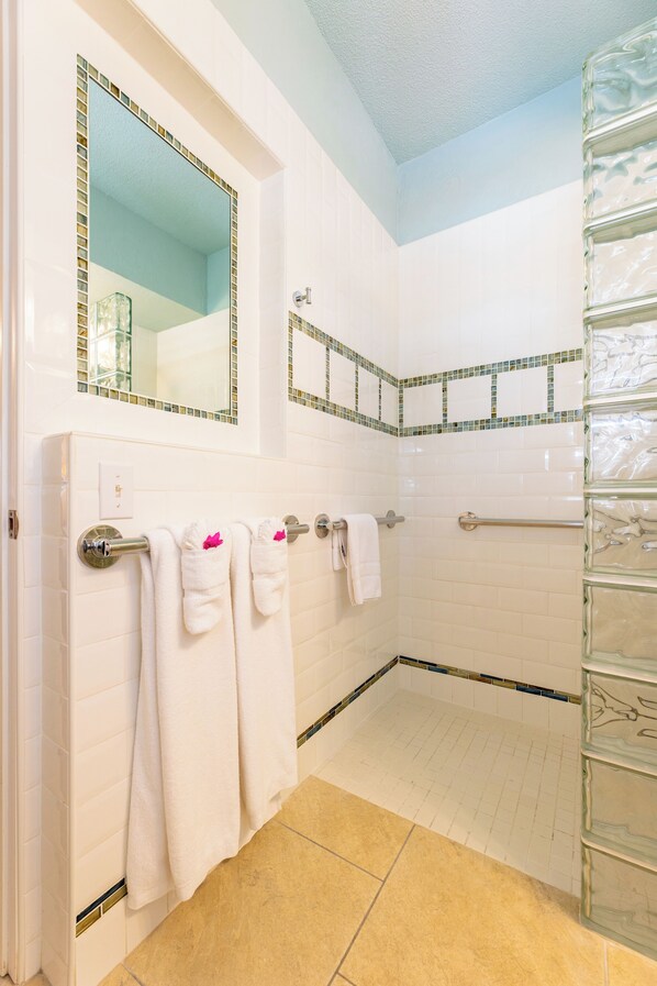 A bathroom with white tiles, a glass shower enclosure, and a mirror with a mosaic border.