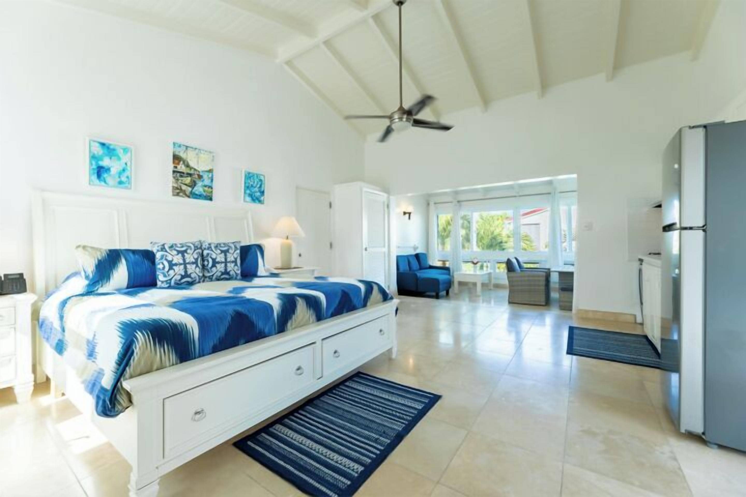 A bedroom with a bed, bedside tables, a ceiling fan, and a view into the living area.