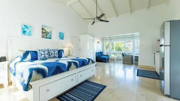 A bedroom with a bed, bedside tables, a ceiling fan, and a view into the living area.